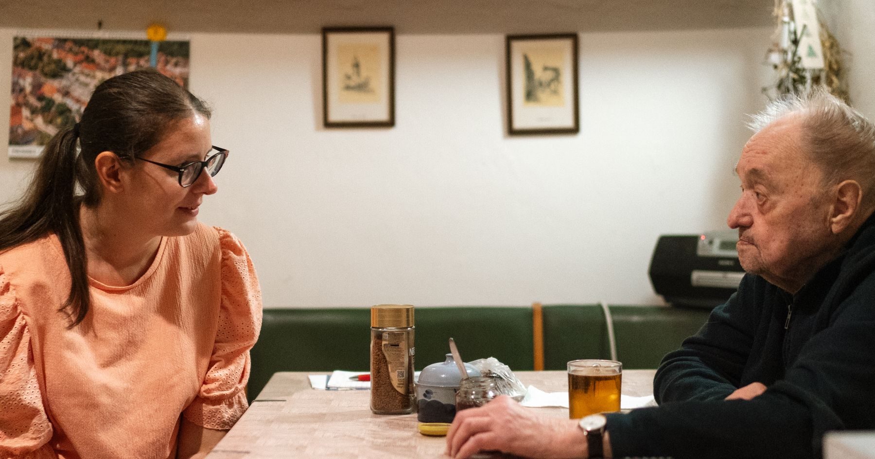 A younger woman and an older man talking across a kitchen table